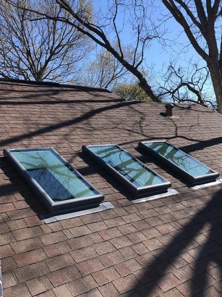 Three skylights on a roof with trees in the background.